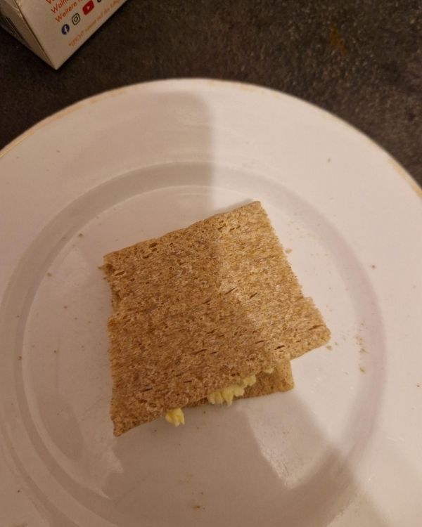 Das Bild zeigt ein zusammengelegtes Knäckebrot mit Butter auf einem kleinen Teller.