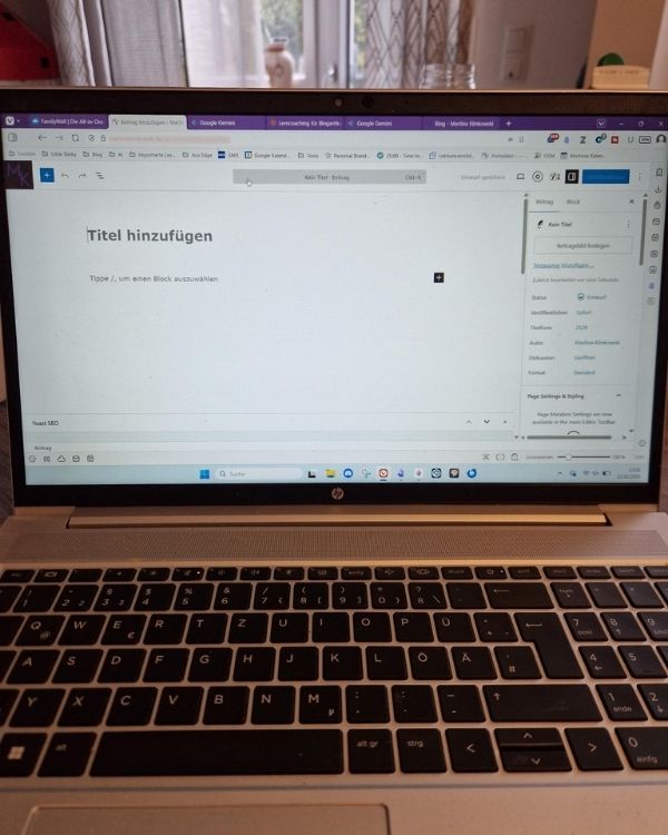 Laptop-Bildschirm mit einem leeren Blogartikel und der Aufforderung 'Titel hinzufügen' und einem leeren Platzhalter-Block. Im Hintergrund ist ein Fenster mit Vorhängen zu sehen.